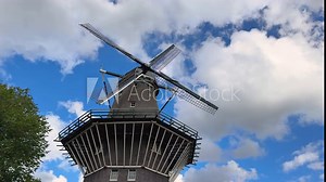 Traditional Dutch wind mill. Popular tourist landmark in the Amsterdam. Windmill spin in the wind on the blue sky background with clouds at sunny day